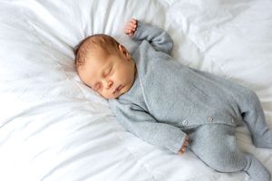 Peaceful newborn baby sleeping in gray knit onesie on white bedding.