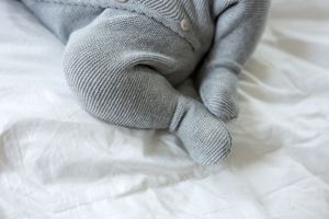 Close-up of newborn baby feet in gray knit onesie on white bedding.