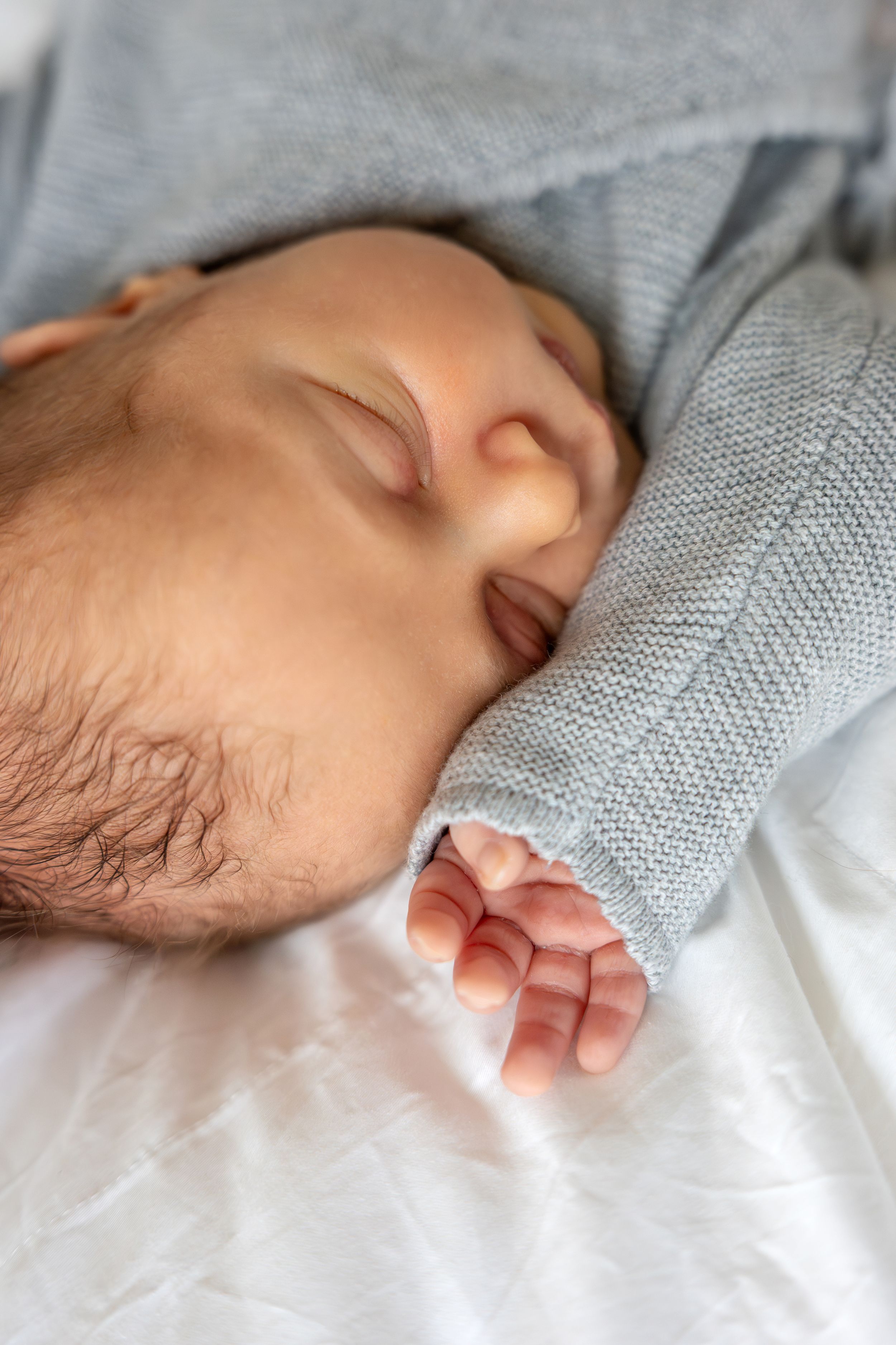 Close-up of sleeping newborn baby face and tiny hand in gray knit sleeper.