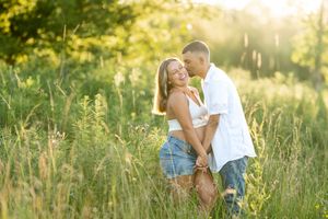 Happy expecting couple embracing and laughing together in a lush green field during a golden hour session.