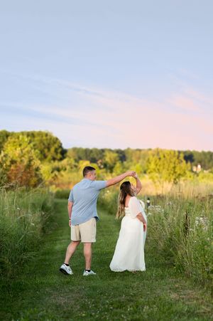 Man spinning pregnant woman in a white maternity dress during a romantic outdoor photoshoot at sunset.