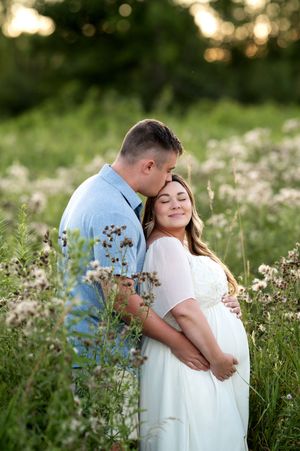 Couple embracing tenderly in a wildflower meadow during a golden hour maternity photography session.