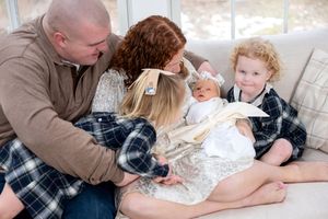 Family of four with a newborn baby and toddler sharing a warm moment together on a couch.