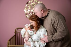 New parents kissing their newborn baby in a pink nursery with gold butterfly wall decor.