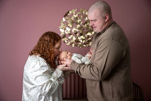 New parents tenderly hold their sleeping newborn baby together in a pink-walled nursery.