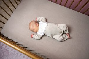 Peaceful newborn baby sleeping on back in a gold crib with neutral bedding.