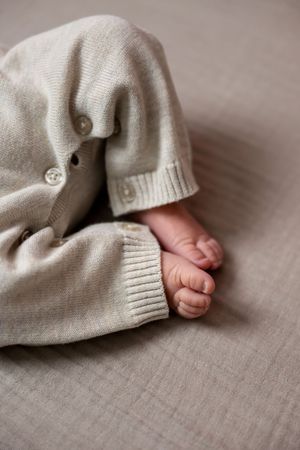 Close-up of tiny newborn baby feet peeking out of a soft beige knit romper.