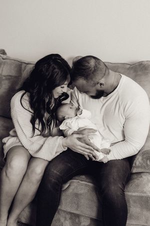 Black and white photo of new parents on a couch sharing a tender moment with their newborn.