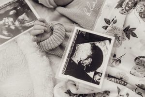 Black and white close-up of a newborn baby hand beside ultrasound photos on a floral blanket.