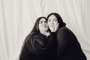 Two young women in black outfits posing together blowing kisses in black and white photo.