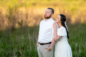 A couple stands in a sunlit green field, woman leaning affectionately against mans shoulder.