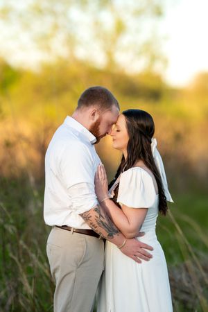 A couple shares a tender almost-kiss moment in a warm golden sunlit outdoor field setting.