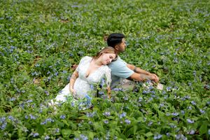 Couple relaxing together in a field of blue wildflowers during a romantic maternity photoshoot.