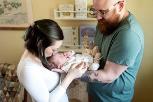 New parents tenderly holding and kissing their newborn baby in a cozy nursery room.