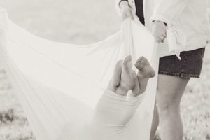 Black and white photo of newborn baby wrapped in white cloth held by parents.