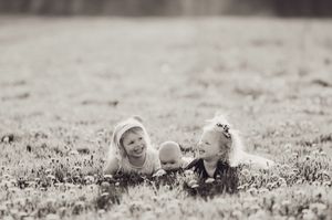 Black and white photo of two girls and baby laughing together in grassy field.