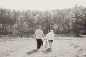 Black and white photo of couple walking hand in hand with child toward tree line.