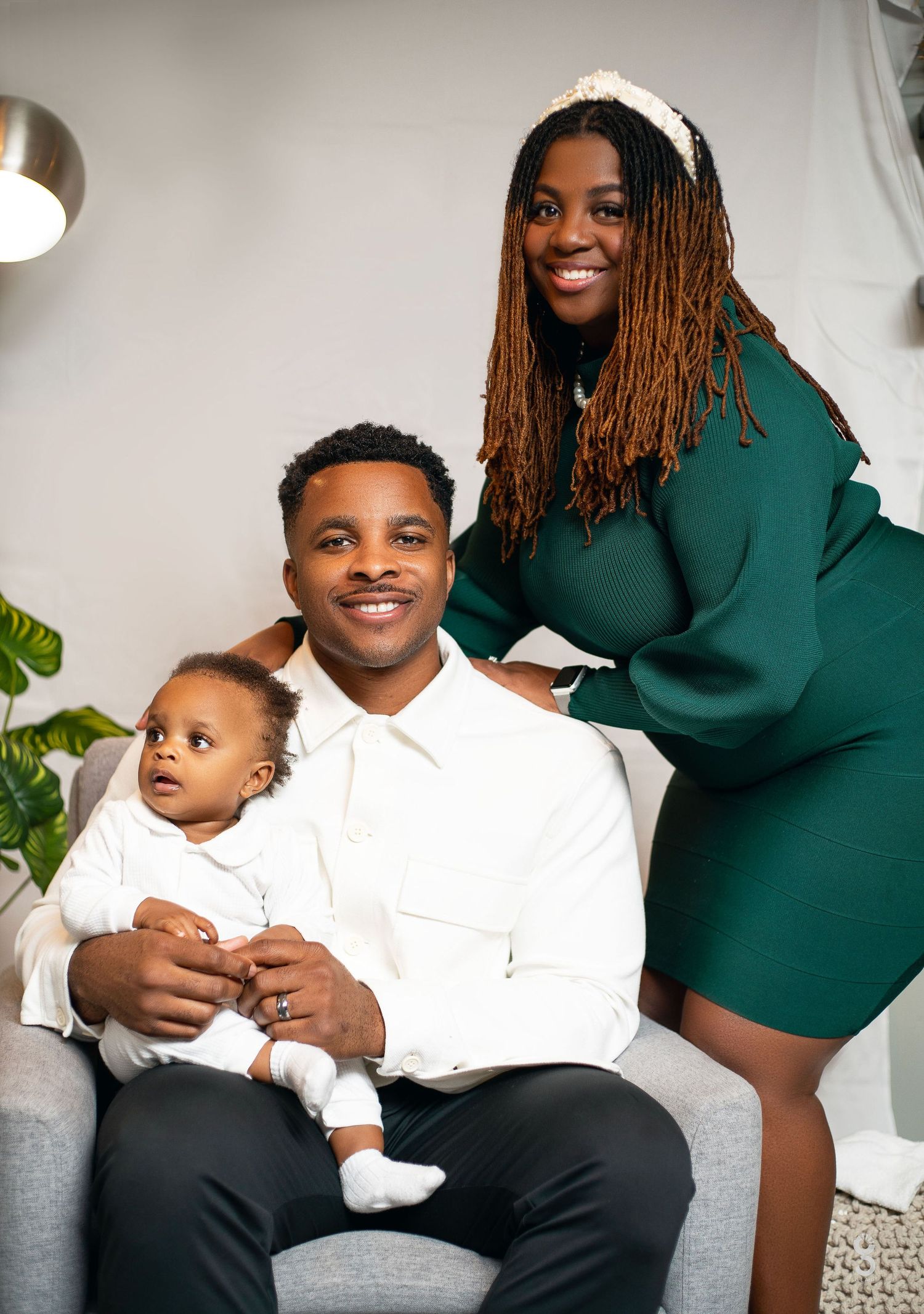 A family portrait showing parents sitting on a couch holding their baby in a home setting.