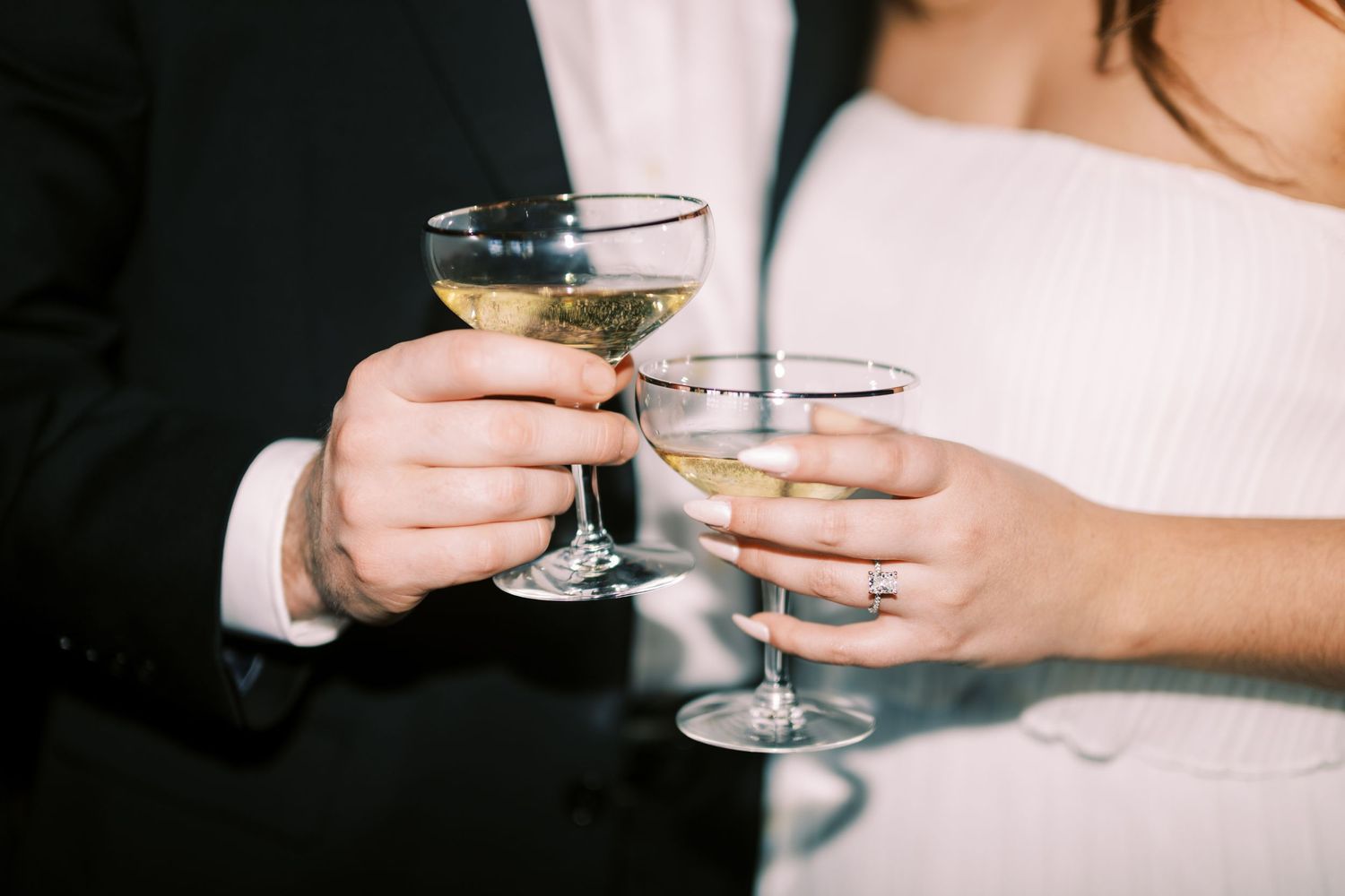 Two hands holding champagne glasses toast in a celebratory moment.