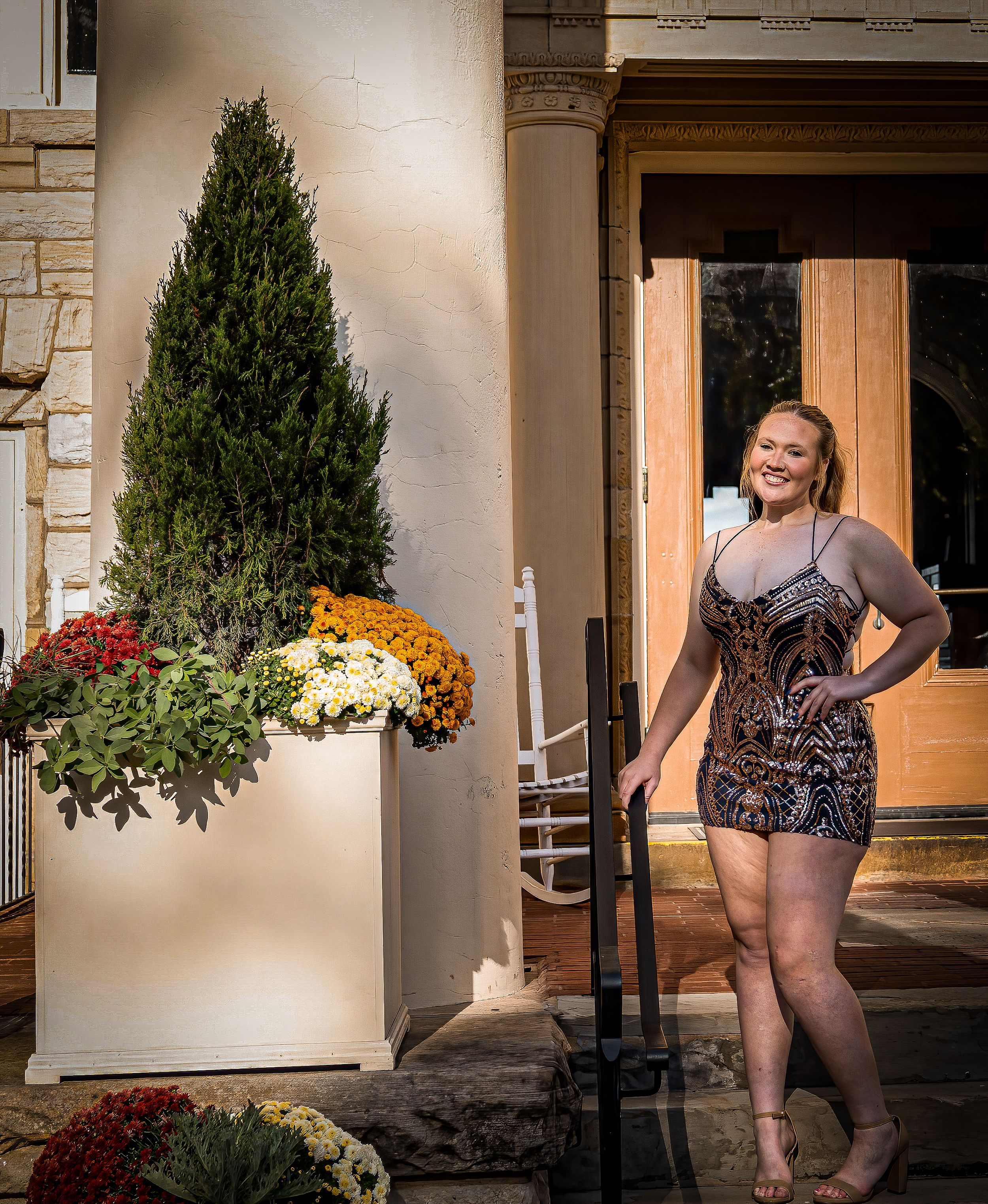 A person poses in a sequined dress next to fall decorations and potted mums on a front porch.
prom 
riverside