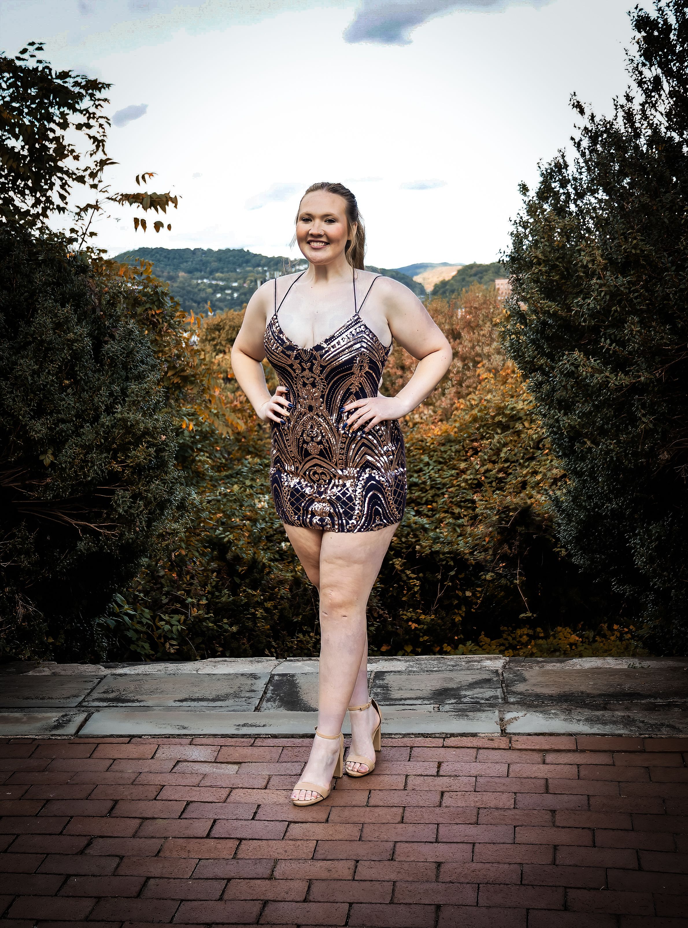 A person in a patterned mini dress poses confidently on brick pavers with autumn foliage in background.
prom 
riverside