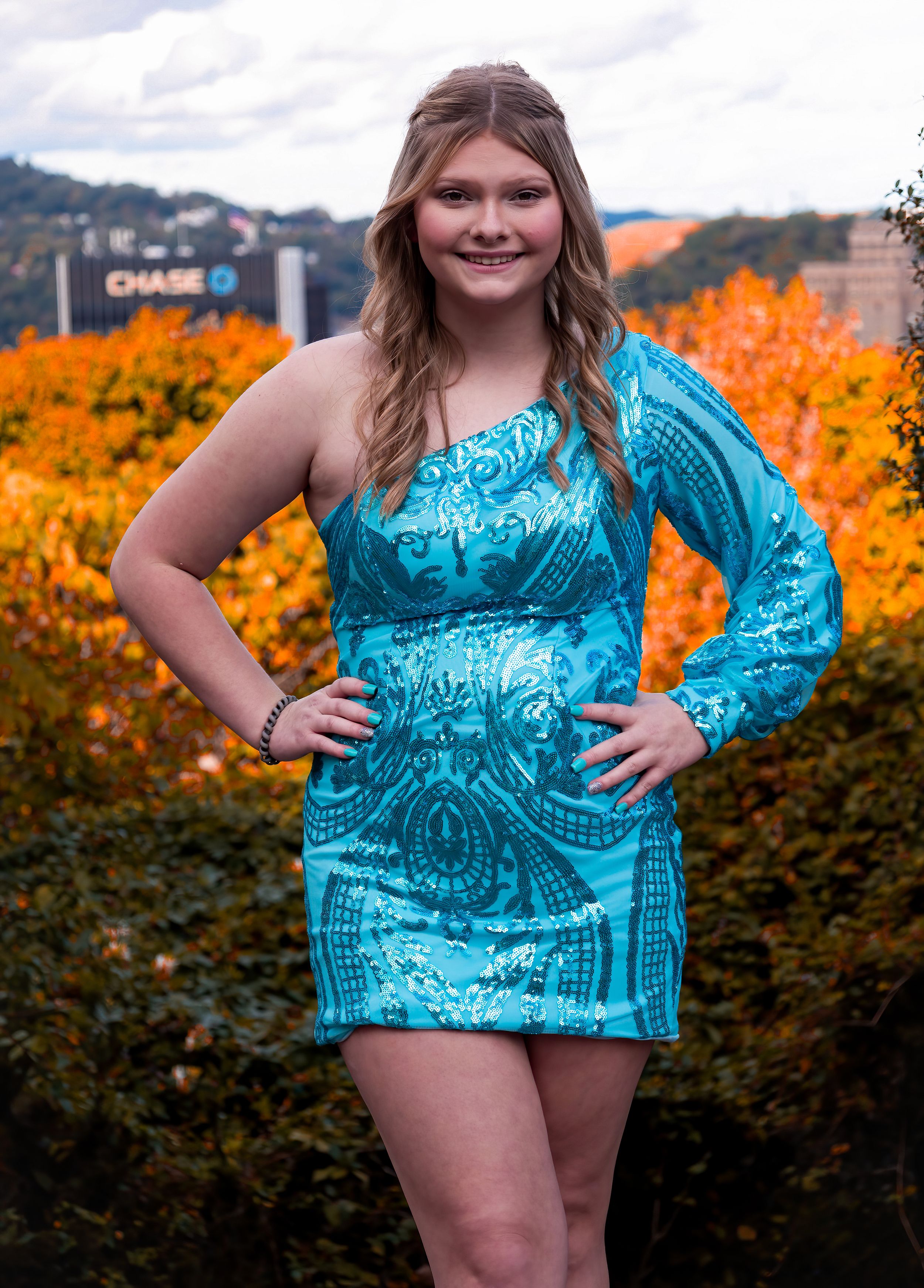 A person wearing a turquoise one-shoulder dress poses against vibrant orange fall foliage.
prom 
riverside