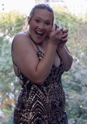 A woman in a sparkly dress displays excited expression while holding something in her hands outdoors.
prom 
riverside