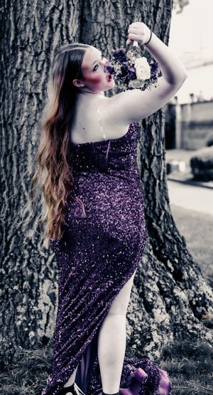 A person in a sparkly purple formal dress poses against a tree trunk while holding flowers.
prom 
riverside