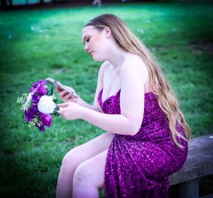 A person in purple sequin dress sits examining a bouquet of flowers in an outdoor setting.
prom 
riverside