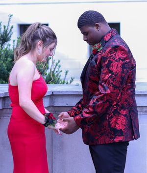A couple shares a tender moment in formal attire with red dress and floral jacket.