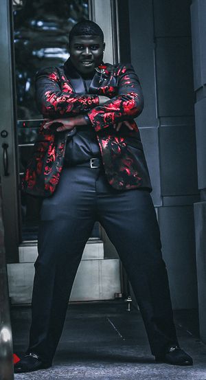 Stylish pose in red and black floral jacket with black dress pants against doorway.