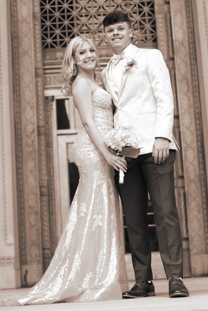 A couple poses for a formal portrait in front of an ornate door, wearing a sparkly gown and white suit jacket.