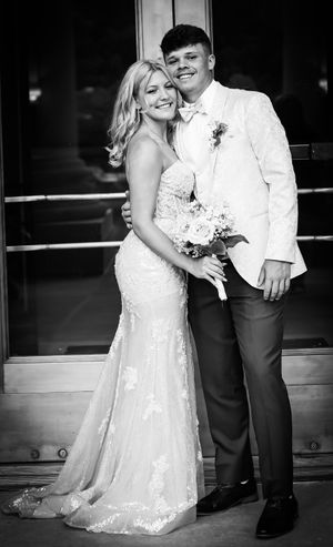 A black and white formal portrait of a couple in elegant attire smiling at the camera.