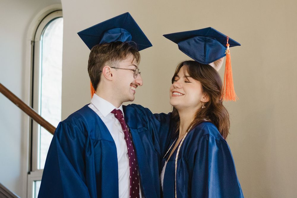Two graduates in blue caps and gowns share a joyful moment during graduation ceremony.