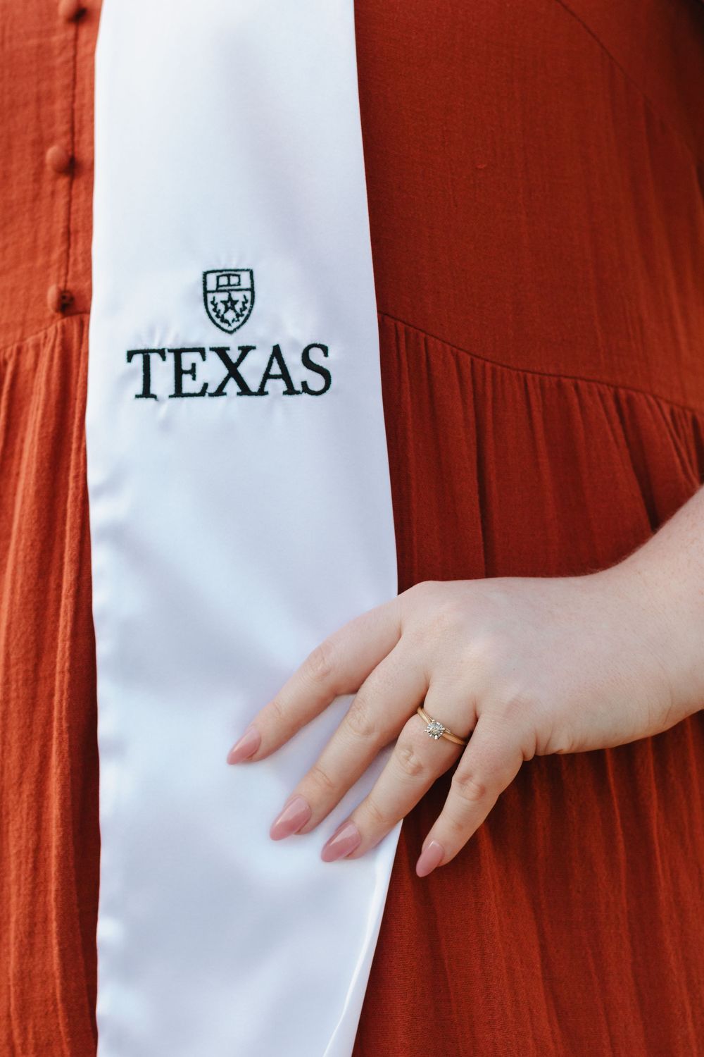 A hand wearing an engagement ring rests against orange fabric next to a white Texas university logo stripe.