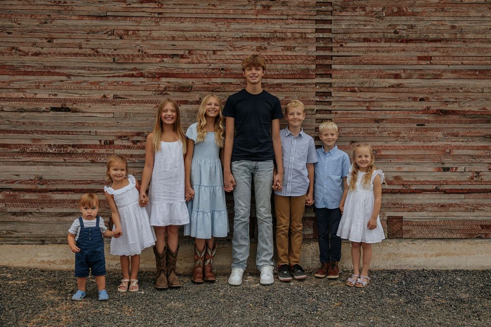 Children and adults lined up against a rustic wooden barn wall for a family photo.