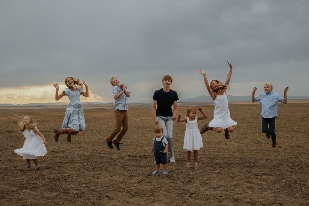 Children jumping and playing together on an open field at sunset.