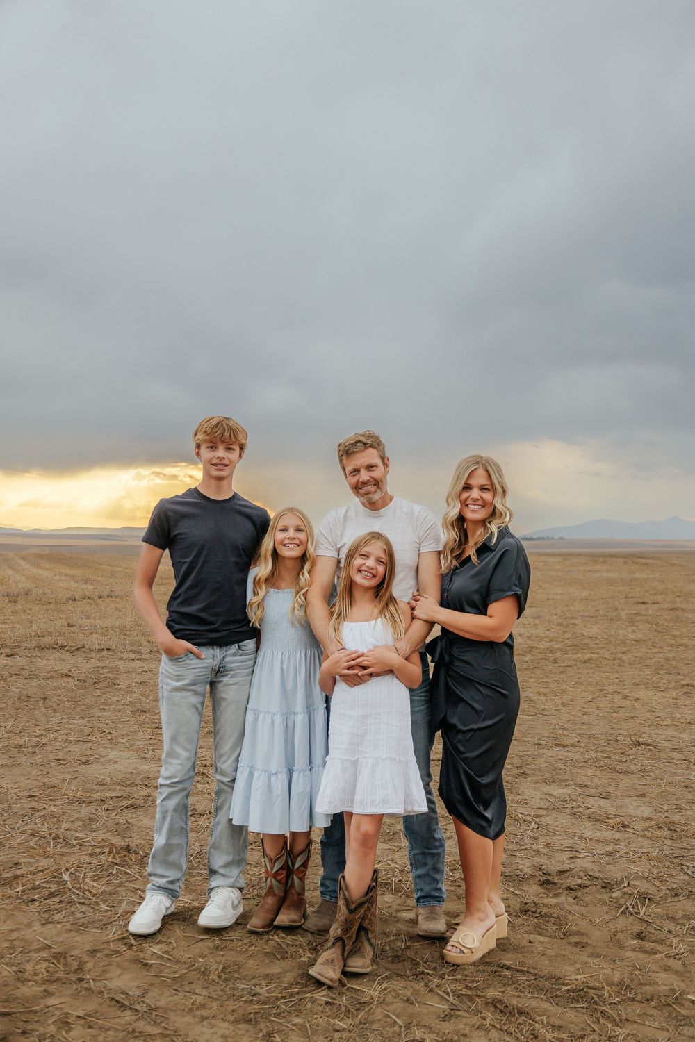 Family group photo on a desert plain with dramatic cloudy sky at sunset.