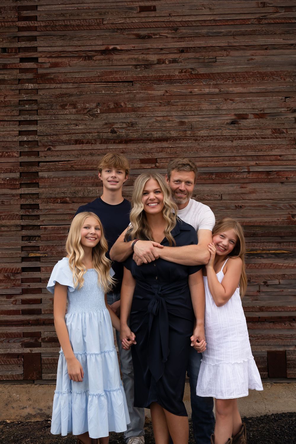 Family group photo against weathered wooden barn siding.