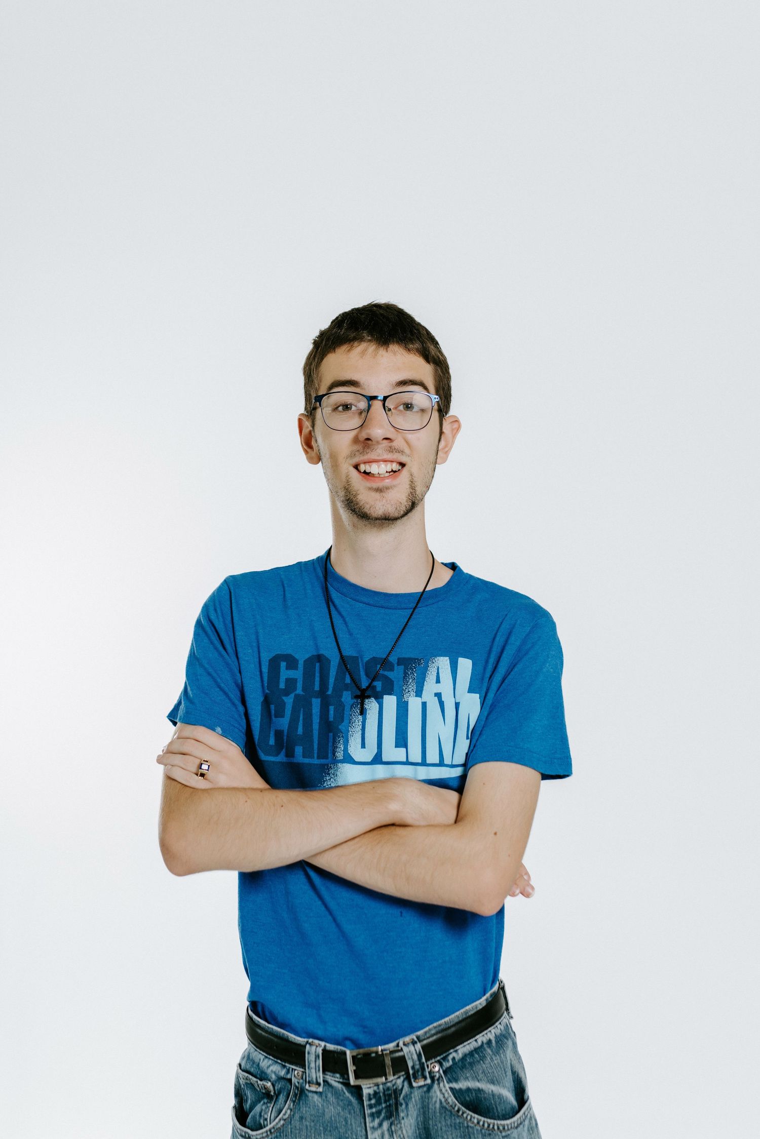 Person wearing glasses and a blue Coastal Carolina t-shirt poses with crossed arms and a friendly smile.
