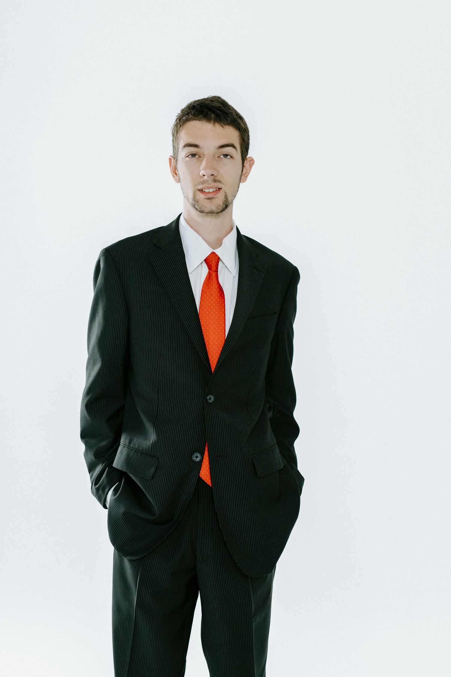 Professional portrait of someone wearing a black suit and bright orange tie against a white background.
