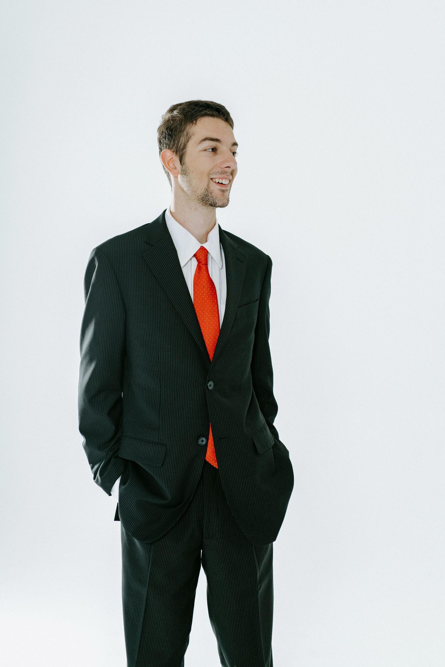 Professional wearing black suit and red tie stands in dynamic poses against white background.