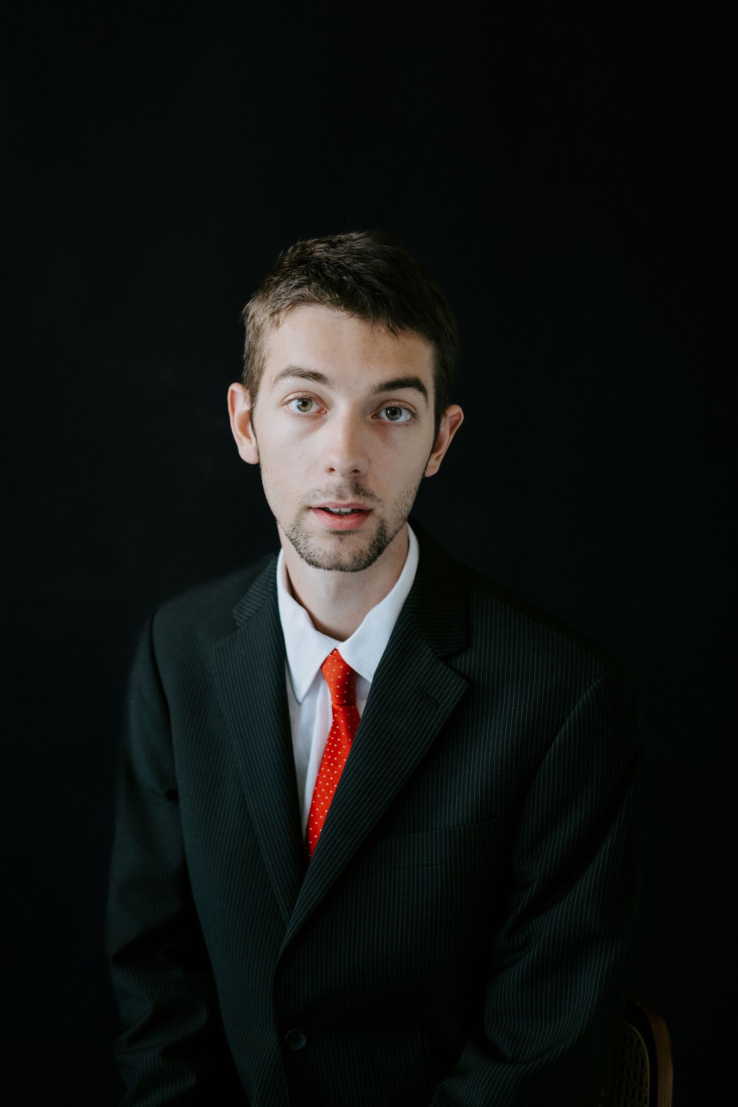 Professional portrait series showing someone in a dark suit and red tie against a black background.