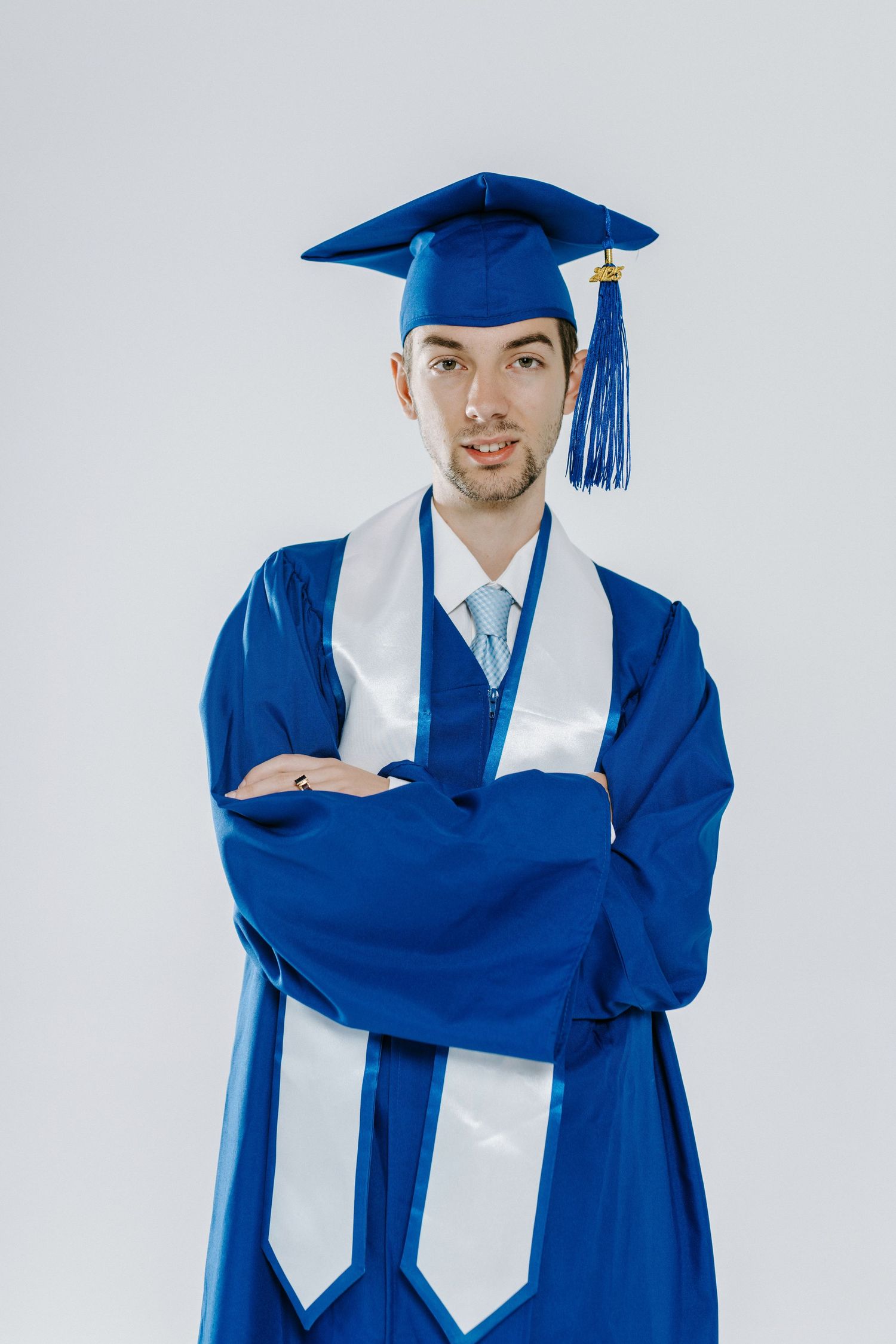 Graduate in royal blue cap and gown with white stole poses confidently against white background.