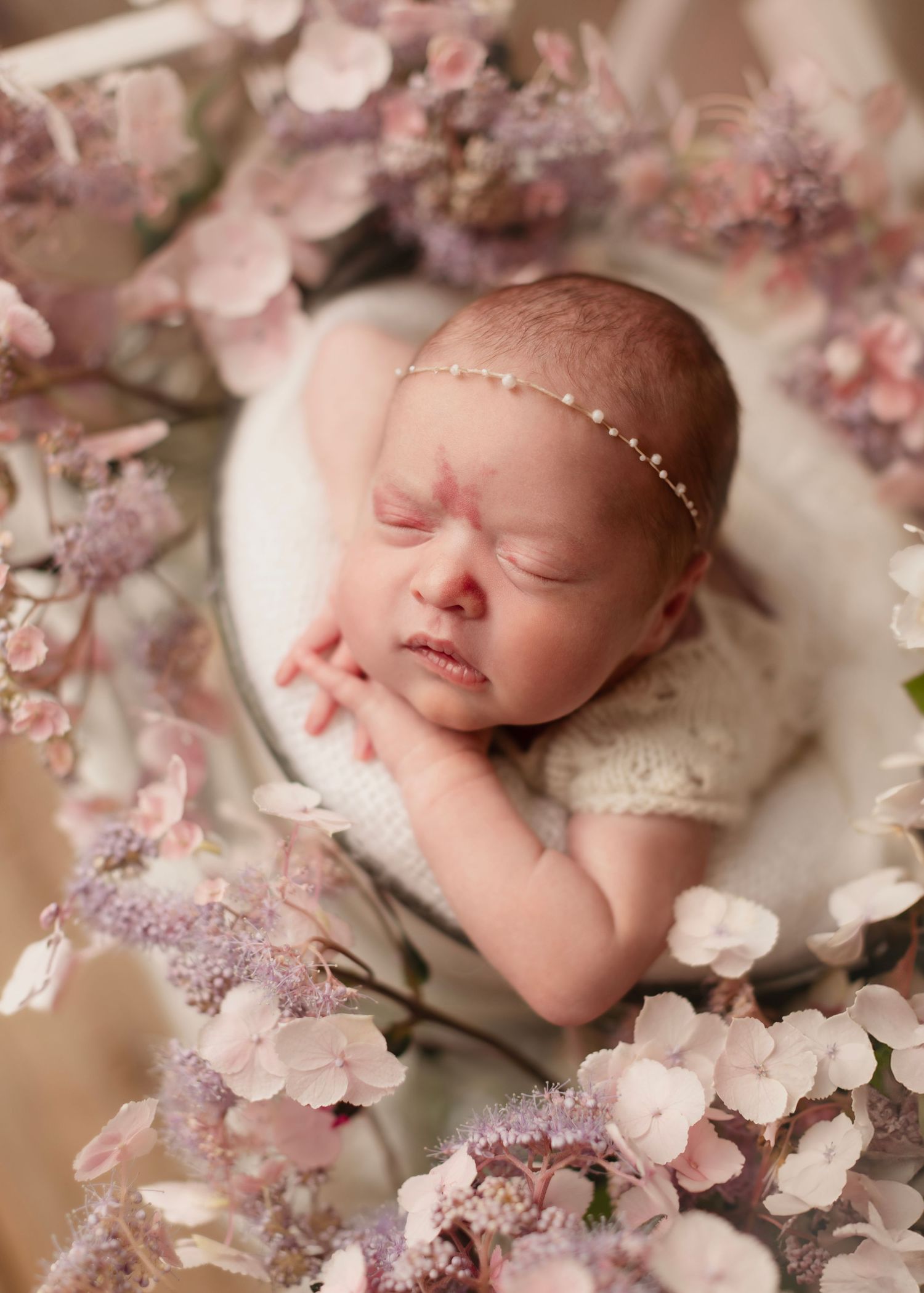 Sleeping newborn nestled among delicate pink cherry blossoms in a dreamy spring-themed portrait setting.