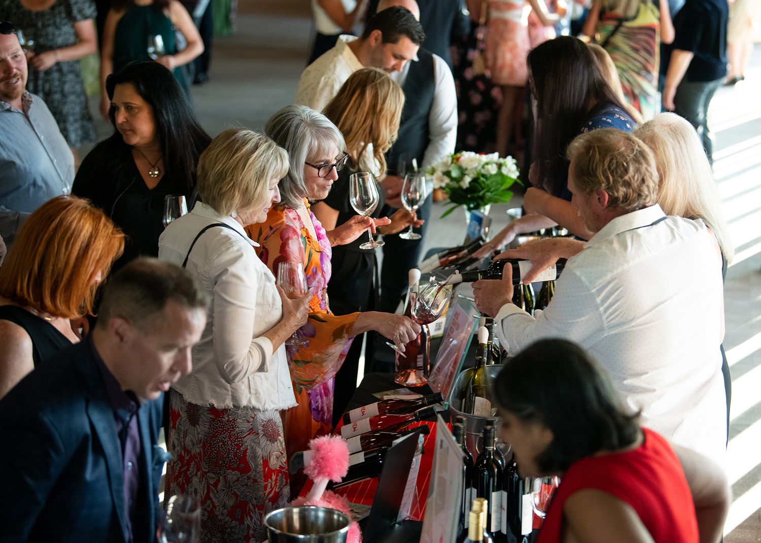 Guests gathered around wine tasting tables at a busy wine event.