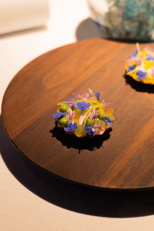 Colorful edible flowers and garnishes artfully arranged on a dark wooden circular plate.