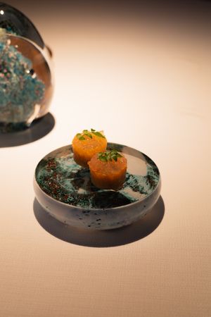 Orange spherical dish garnished with green powder on a black circular plate.