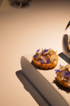 Artistically plated dish with purple edible flowers and garnishes on a textured surface.