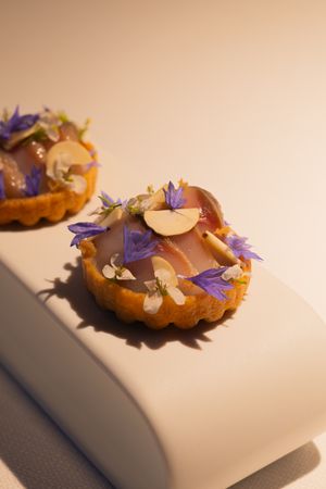 Elegant pastry dish adorned with purple flowers and delicate garnishes on a white surface.